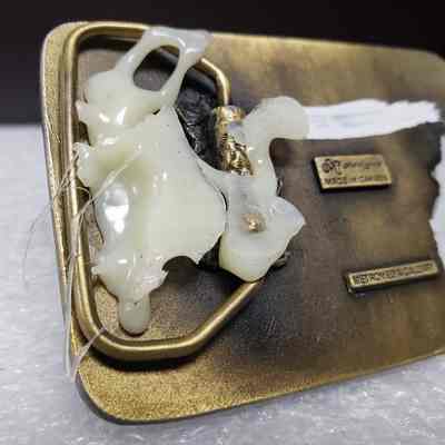 [Belt Buckle] Triton Project Inc./Nova/Cooper Industries, Clarkson Valley Compressor Station, 1991, Antique Bronze - Back, Close-Up: Close-up view of hot glue attached to hinge on back.