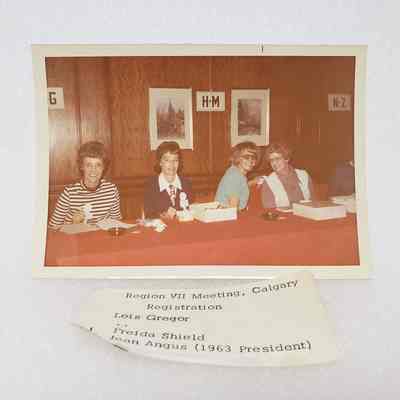 [Photo] Lois Gregor, Freida Shield and Jean Angus Seated at Red Table, Region VII Meeting Calgary, Association of Desk and Derrick Clubs, Landscape, White Border, c.1972