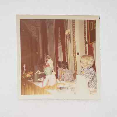 [Photo] Four Ladies Seated at Yellow Table Facing Lady Standing at Podium, Association of Desk and Derrick Clubs, Square, White Border, c.1972