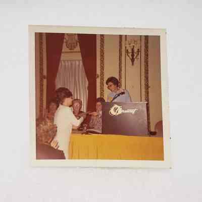 [Photo] Lady in White Receiving Award from Lady at Podium, Association of Desk and Derrick Clubs, Square, White Border, c.1972