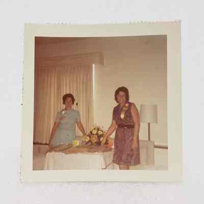 [Photo] Two Ladies Standing Beside a Table With Dishes and Bouquet, Association of Desk and Derrick Clubs, Small, Square, White Border, c.1972