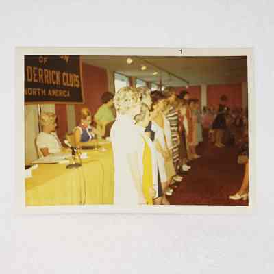 [Photo] Line of Women Standing in Front of a Yellow Covered Table, Association of Desk and Derrick Clubs of North America, c.1971