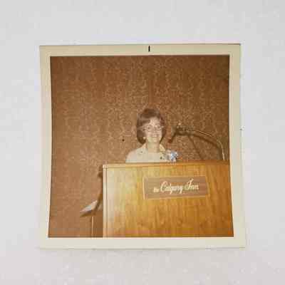 [Photo] Rae Valerio Standing at Podium, The Calgary Inn, Association of Desk and Derrick Clubs, Square, White Border, c.1972