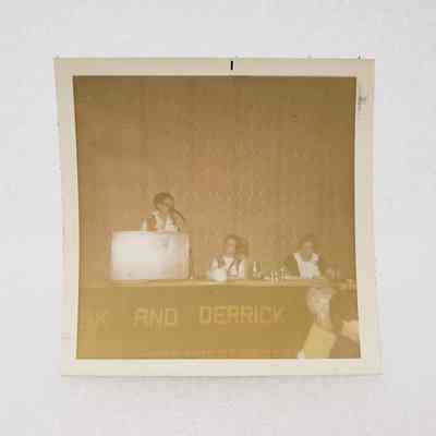 [Photo] Lady Speaking at Podium with Two Ladies Seated at Panel, Association of Desk and Derrick Clubs, Square, White Border, c.1972