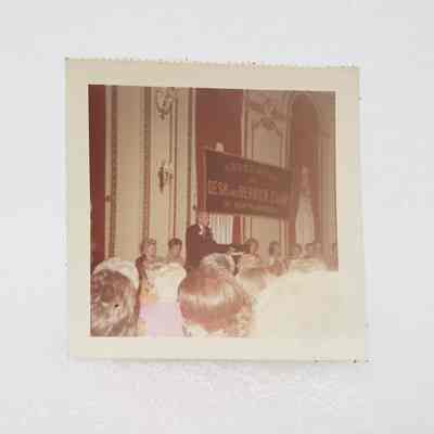 [Photo] Man Standing at Podium with Ladies at Panel Table and Backs of Heads, Association of Desk and Derrick Clubs, Small, Square, White Border, c.1972
