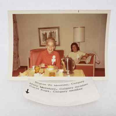 [Photo] Mary McIntyre and Carol Rugg Seated at Yellow Table and Red Couch, Region VII Meeting Calgary, Association of Desk and Derrick Clubs, Landscape, White Border, c.1972