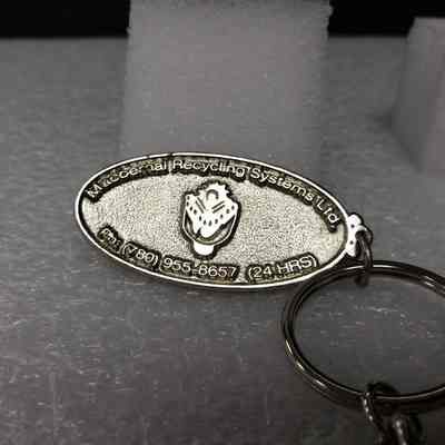 [Keychain] Macbernal Recyling Systems Ltd., Drill Head, Silver - Angled, Oval Fob: Angled view of oval fob to highlight 3D text elements.