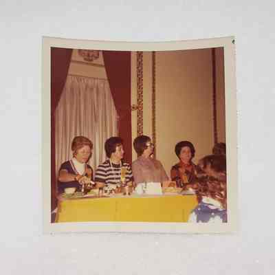 [Photo] Four Ladies Seated at Yellow Table, Association of Desk and Derrick Clubs, Square, White Border, c.1972