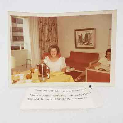 [Photo] Marie Anne White and Carol Rugged seated at Yellow Table and Red Couch, Region VII Meeting Calgary, Association of Desk and Derrick Clubs, Landscape, White Border, c.1972