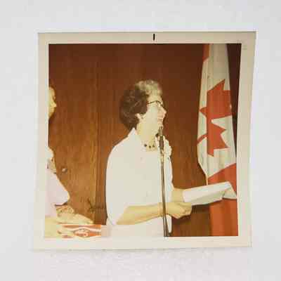 [Photo] Lady Speaking at Microphone with Canadian Flag to Right, Association of Desk and Derrick Clubs, Square, White Border, c.1972
