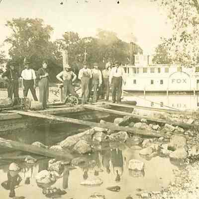 Men on a river, boat with the word "FOX" in background