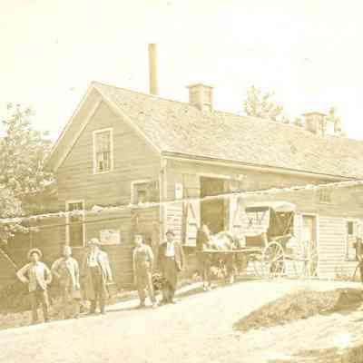 Group of men in front of building with two buggies