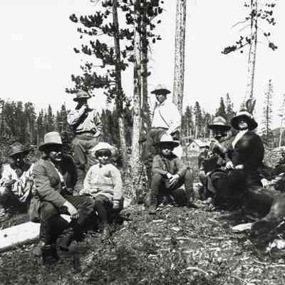 Coe_Family_020: Mai Coe sitting on a log outdoors with seven other people