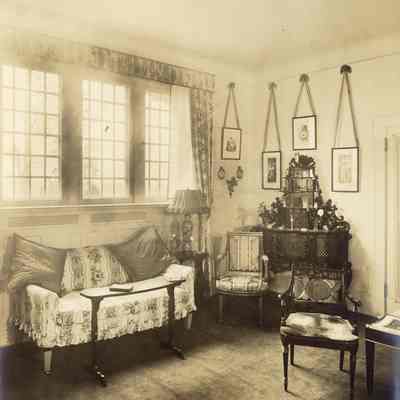 Byrne_031: Interior of room with sofa under window, hanging photos/prints, and chairs, photographed by August Patzig