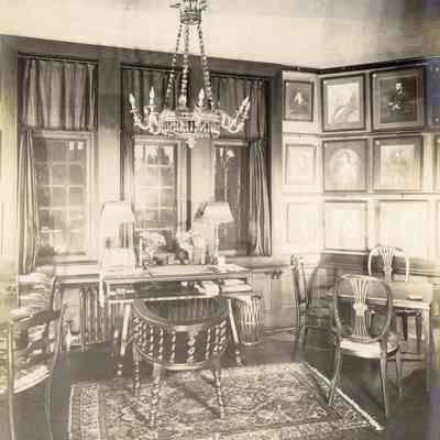 Byrne_032: Interior of room with chandelier, desk under window, and chairs at square tables, photographed by August Patzig