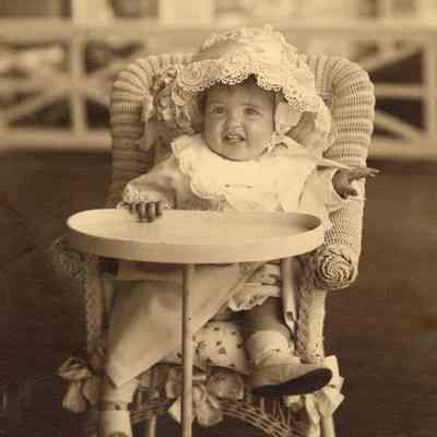 Coe_Natalie_006: Natalie Coe as a baby sitting in wicker high chair and wearing bonnet