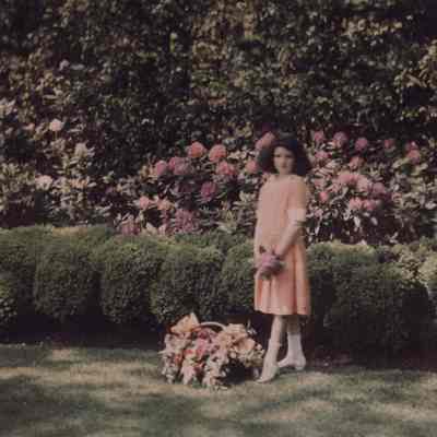 Coe_Natalie_019: Natalie Coe with basket of flowers in front of hedges and flower bushes