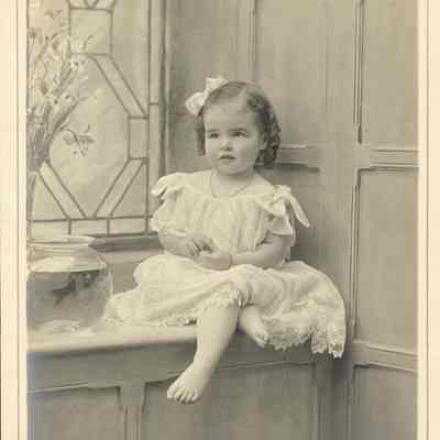 Coe_Natalie_055: Portrait of barefooted Natalie Coe sitting on window ledge next to goldfish bowl, photographed by Sheaight Limited