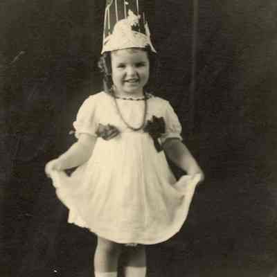 Coe_Natalie_056: Portrait of smiling Natalie Coe holding hem of dress and wearing hat; includes handwritten note from Mai Coe on backside