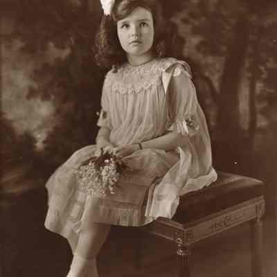 Coe_Natalie_060: Portrait of a seated Natalie Coe holding small bouquet of flowers, photographed by Kazanjian