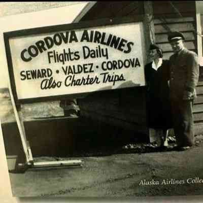 Pilot and flight attendant standing by sign "Cordova Daily Flights Daily - Seward, Valdez, Cordova - Also Charter trips: Digital copy only (From Elizabeth K.'s book - 1 C)