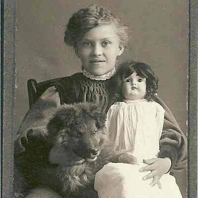 unidentified young girl holding dog and doll while sitting on chair
