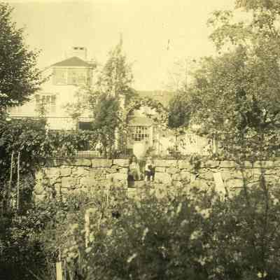 Garden with stone wall, 2 children on steps, house in background at "The Hill"