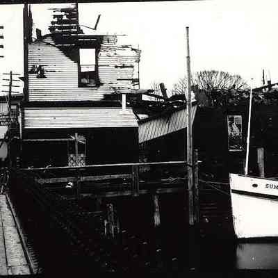 Burned out buildings on river with boat "Summer Girl" in foreground, Mystic CT