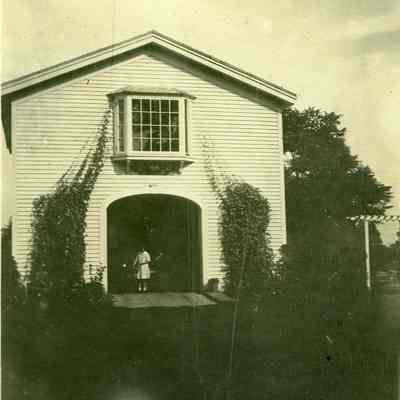 Carriage house with young woman in doorway at "The Hill"