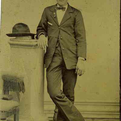 Unknown young man standing with hat on column