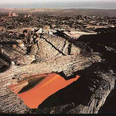 Author's Personal Collection: A skylight, formed when a section of the roof of a lava tube collapses, reveals an active underground flow. The tube insulates the flow, transporting it great distances from the source vent, often to the ocean. J. D. Griggs 1990.