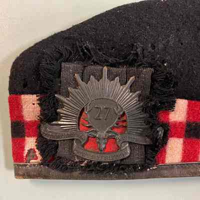 2023.1.2.1: Detail of 27th Battalion unit badge attached to forage cap and moth damage on chequered band.
