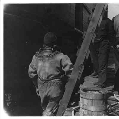 Man in diver's suit and other men standing by vessel