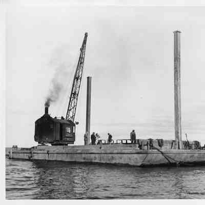 Crane on platform barge being towed by tug boat