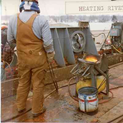 Heating rivet with man in red hard hat 1982