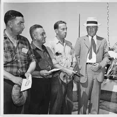Three unidentified male employees in work clothes standing next to LD Smith and ship sponsor