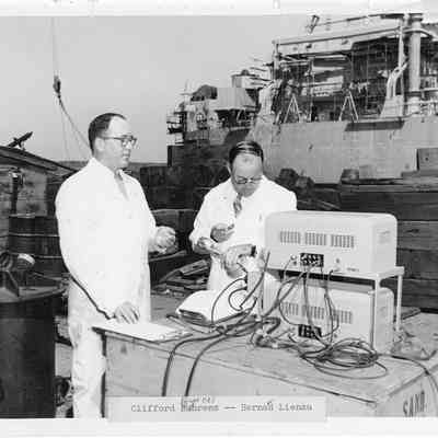 Clifford Byrnes and Bernard Lienau behind wooden box in white coveralls 1954