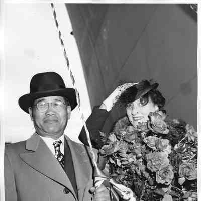 Mrs. Galliane holding flowers alongside man holding christening bottle