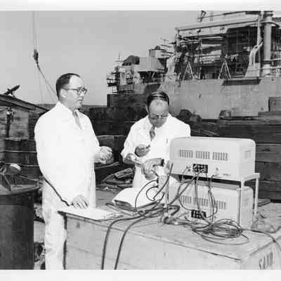 Two men with technical equipment in front of LST-1170, May 22, 1954