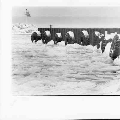 Ten fender tires hanging by chains over water and ice