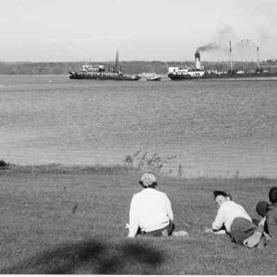 Four people on lawn watching tug between two vessels