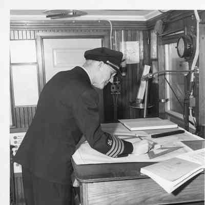 Man making calculations on map in pilothouse of Elton Hoyt II