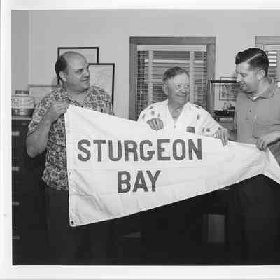 Frank Tachovsky, Captain John Roen, and Roland Berg holding burgee from Sturgeon Bay