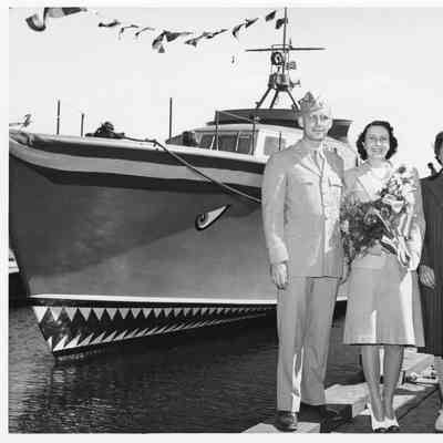 Woman holding flower next to a man and woman with P-571 in background at Peterson Boat Works July 15, 1944