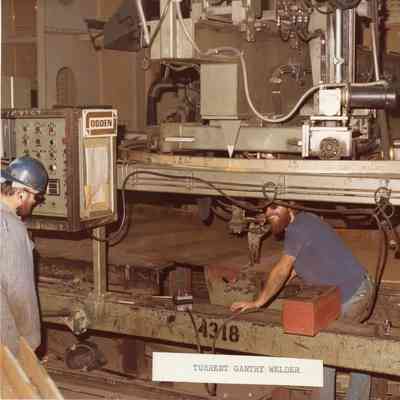 Man at controls, man at welding site of turrent gantry welder
