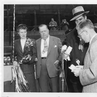 Woman holding christening bottle and man at microphone at christening of Spartan September 6, 1952