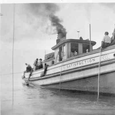 People on deck of Satisfaction docked next to barge
