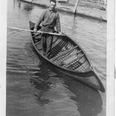 Man standing with oar inside Cupid canoe at Chambers Island Camp