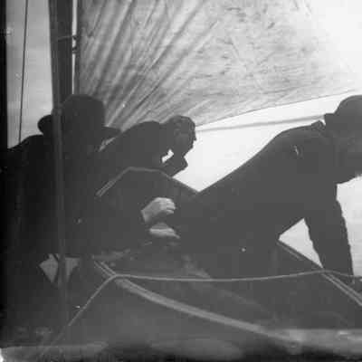 Three men leaning overboard on sailing vessel