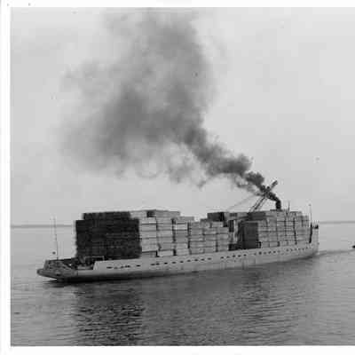 Hilda being pulled by tug with lumber stacked on deck